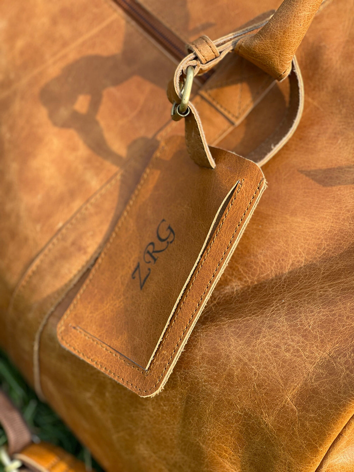 May include: A brown leather duffel bag with a leather luggage tag that says "ZRG" in black lettering.