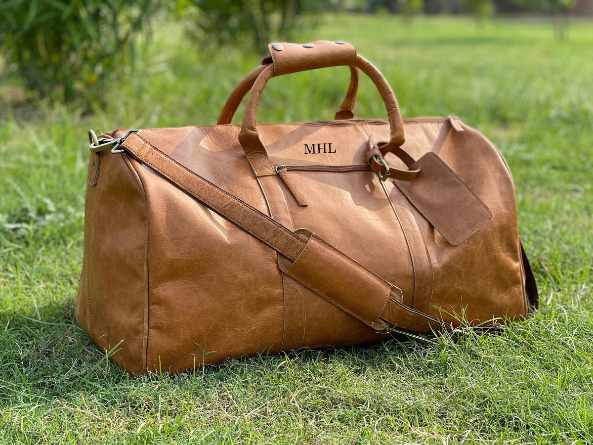May include: A brown leather duffel bag with a top handle and a shoulder strap. The bag has a luggage tag attached to it and the initials "MHL" are embossed on the front.