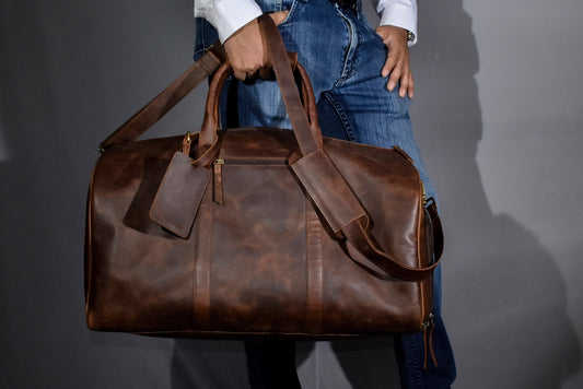 May include: A brown leather duffel bag with a zipper closure and a luggage tag. The bag has a long strap and a shorter handle.