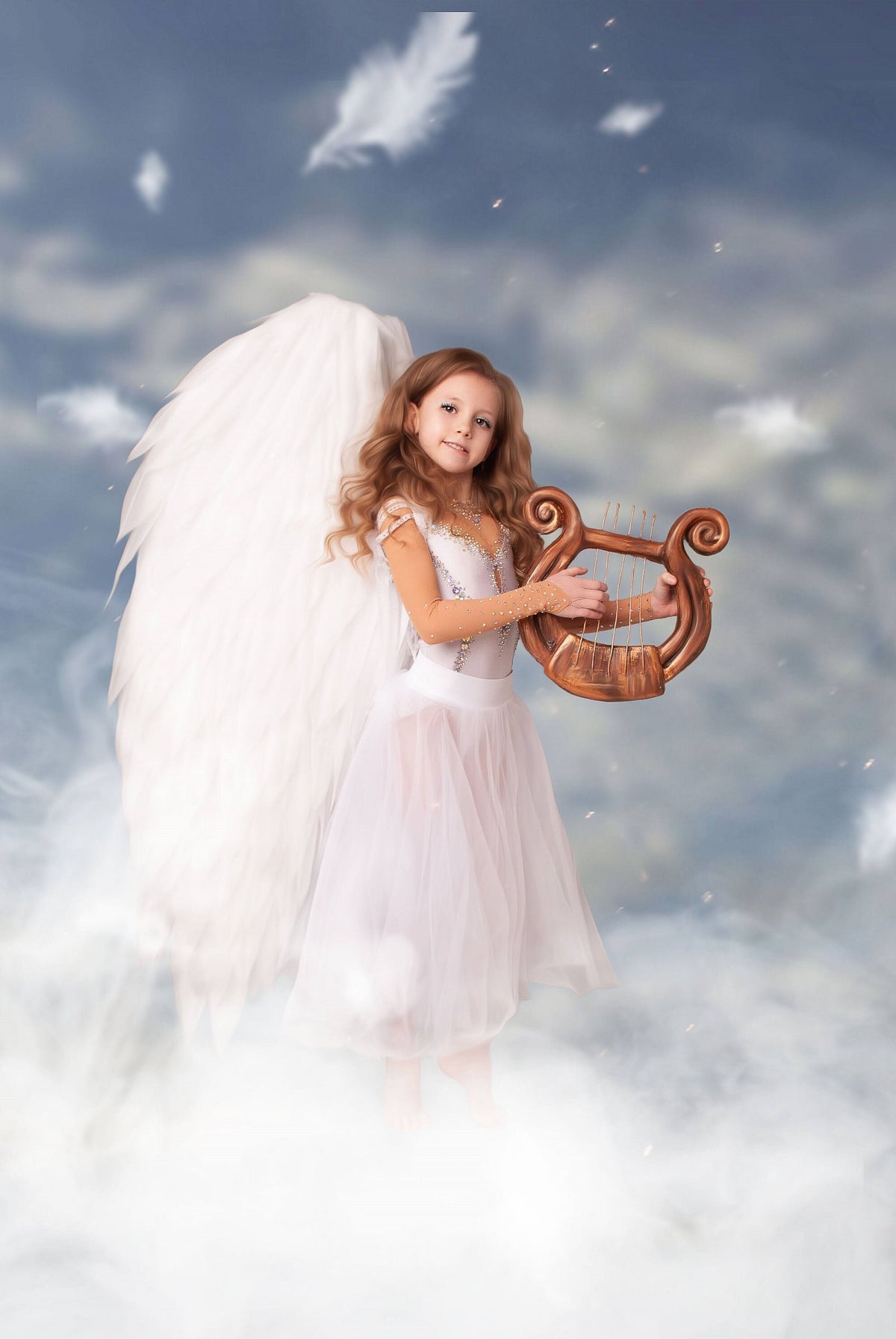 May include: A young girl dressed as an angel with white wings and a white dress, playing a wooden lyre in front of a cloudy sky background.