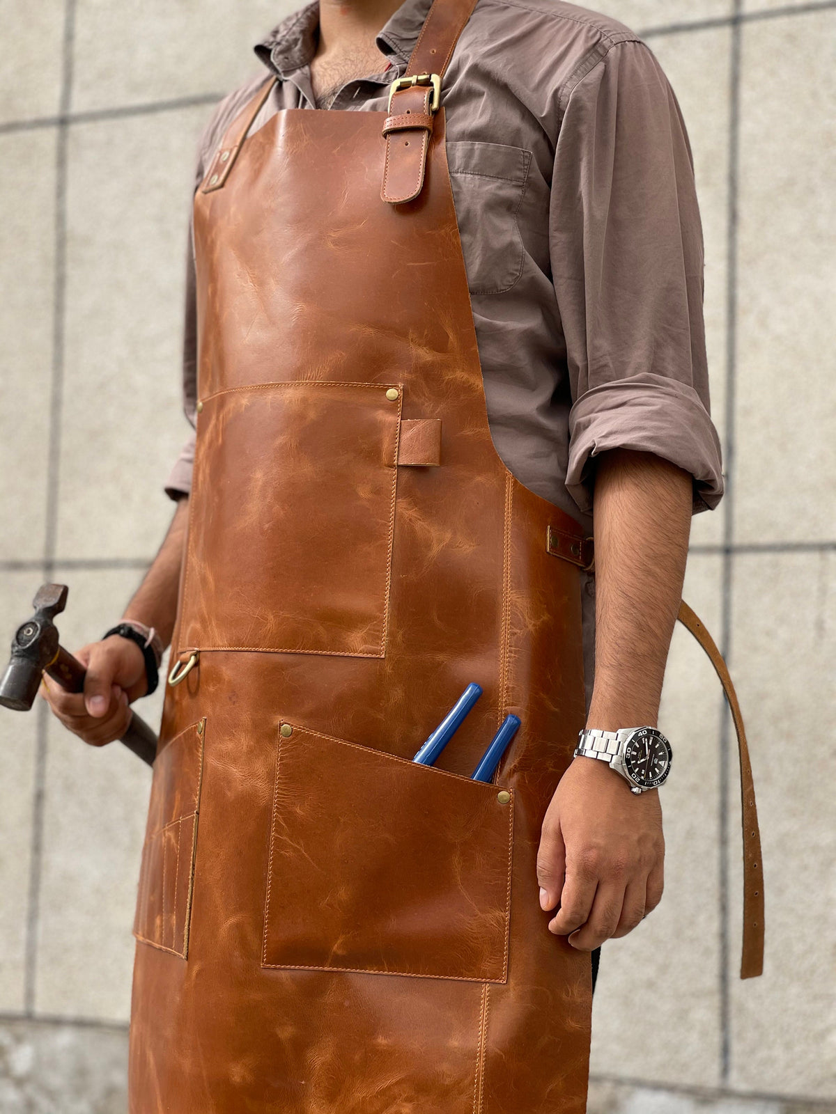 May include: A brown leather apron with multiple pockets and a tool holder. The apron has a brass buckle and adjustable straps.