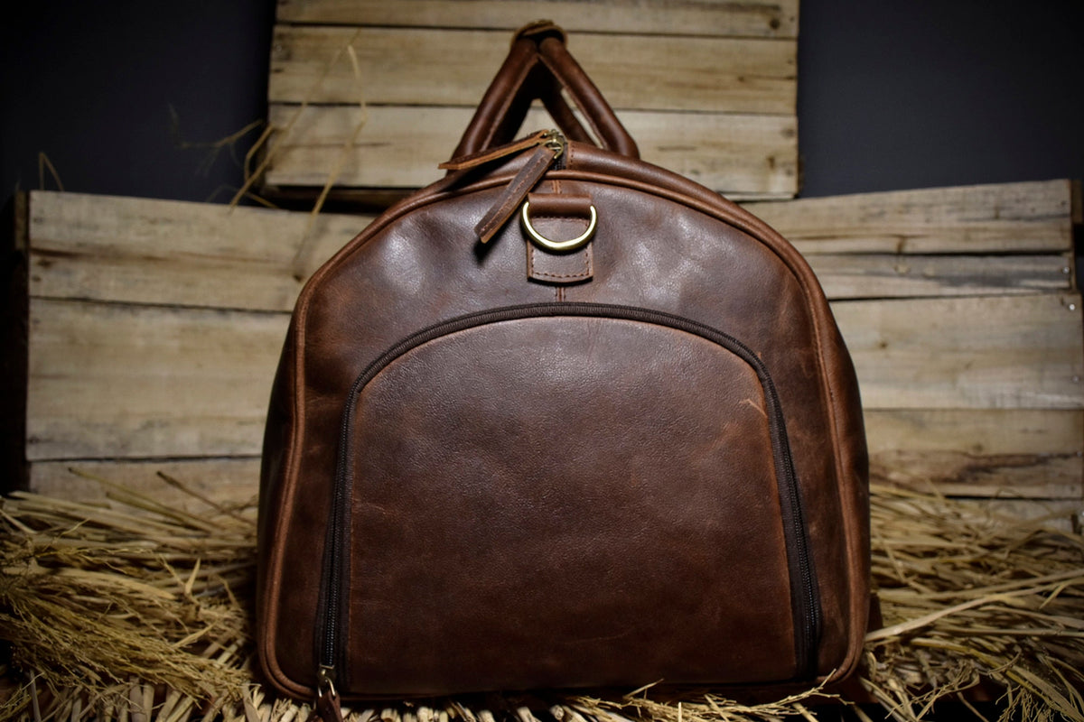 May include: A brown leather duffel bag with a zipper closure and a brass ring handle.