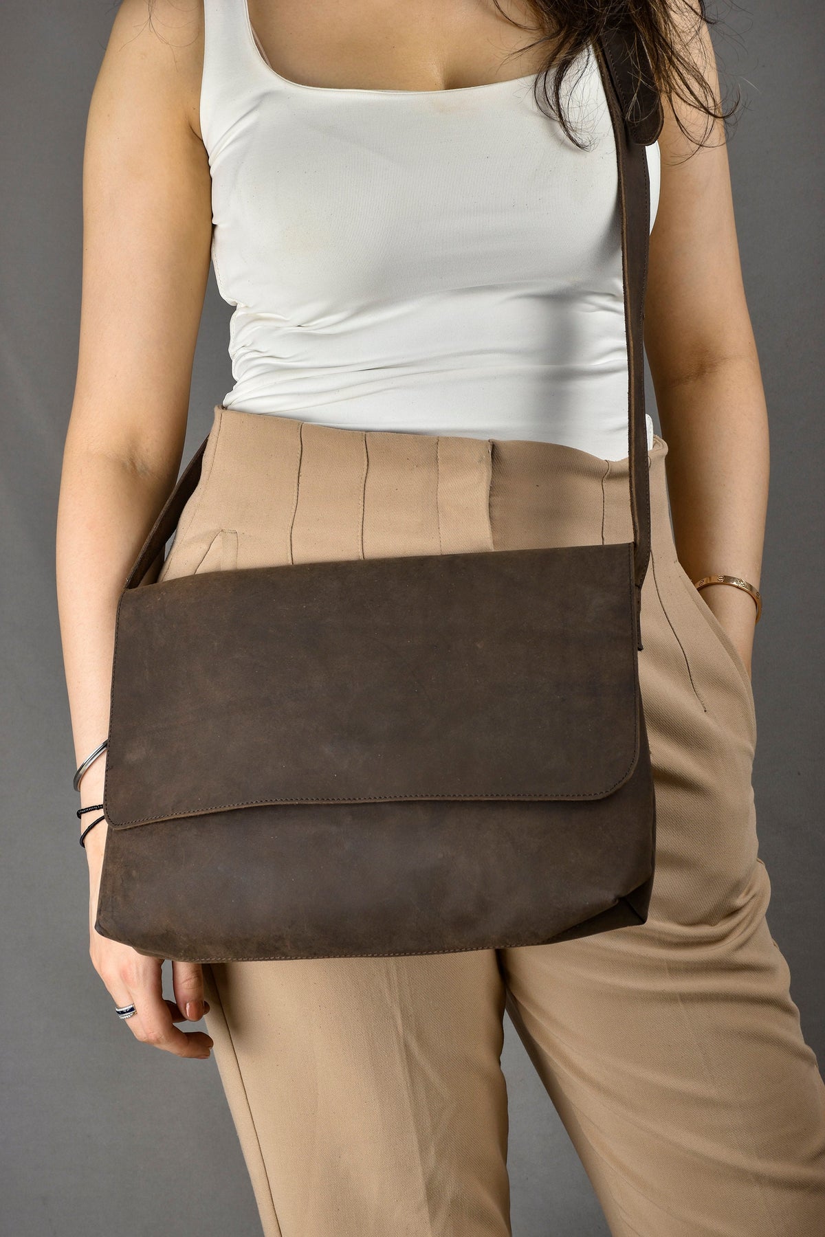 May include: A brown leather messenger bag with a long strap worn over the shoulder. The bag has a flap closure and a single compartment.