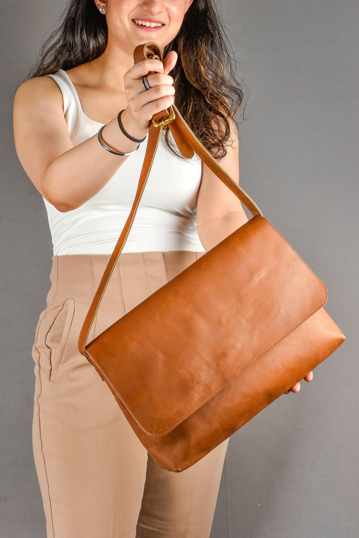May include: A brown leather messenger bag with a long adjustable strap. The bag has a flap closure and a smooth, textured surface.