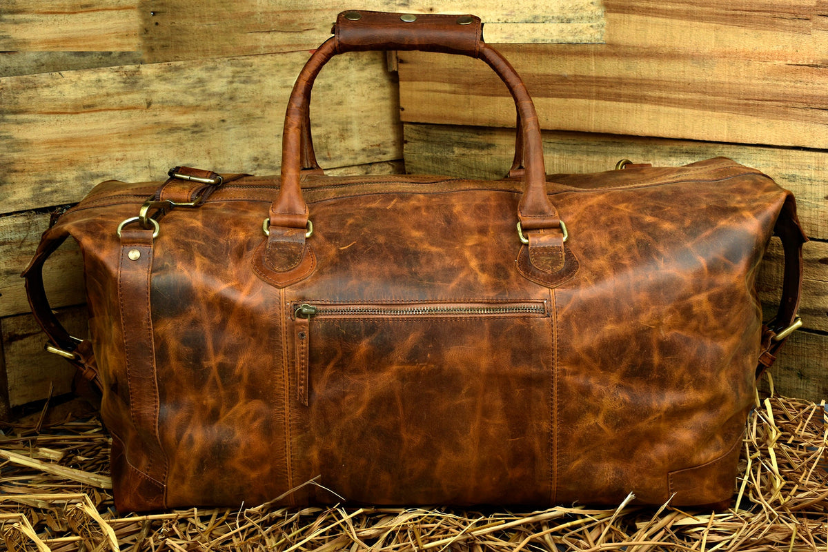 May include: A brown leather duffel bag with a top handle and a shoulder strap. The bag has a zippered pocket on the front.