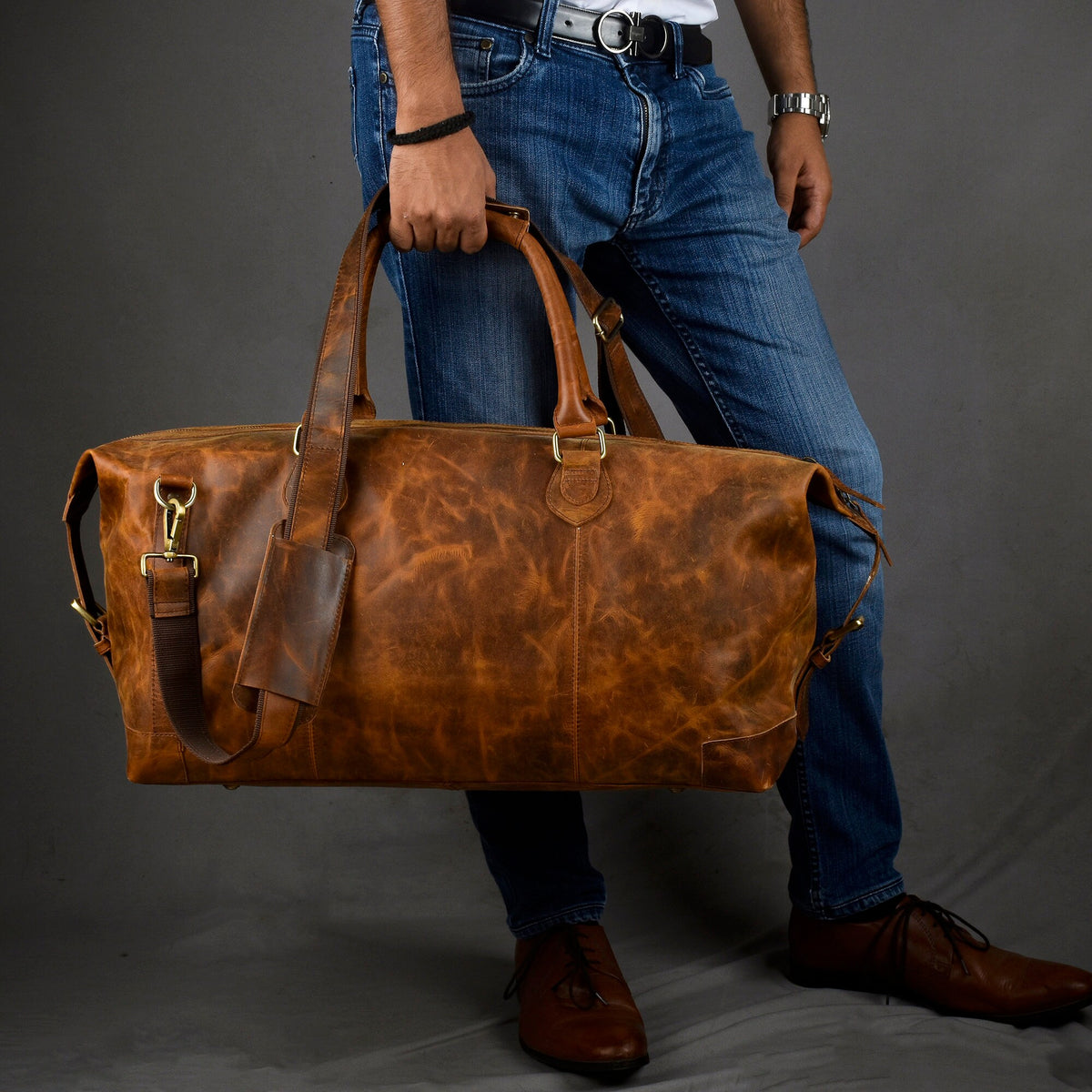May include: A brown leather duffel bag with a top handle and a shoulder strap. The bag has a distressed look and is made of high-quality leather.