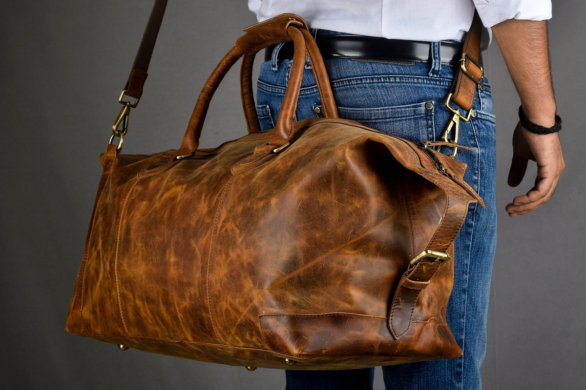 May include: A brown leather duffel bag with a long strap and brass hardware. The bag is worn and has a distressed look.