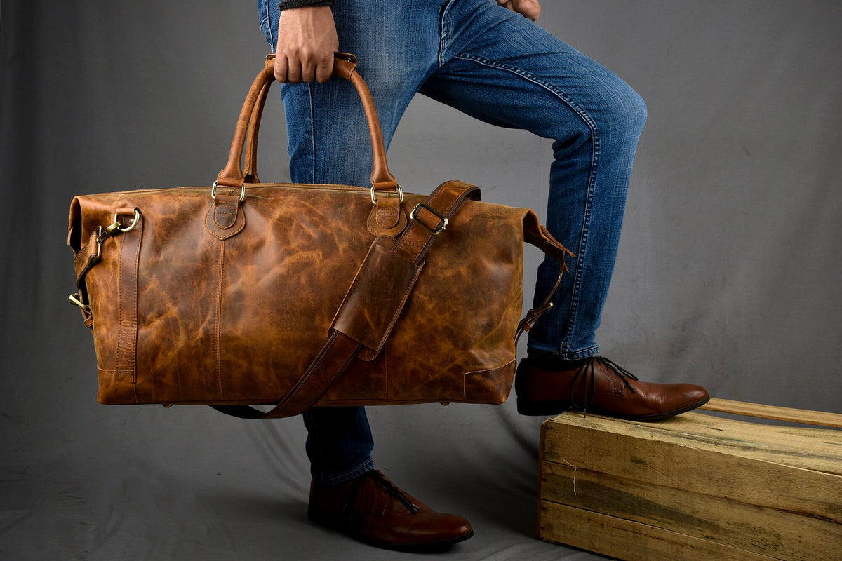 May include: A brown leather duffel bag with a long shoulder strap and two top handles. The bag is worn and has a distressed look.