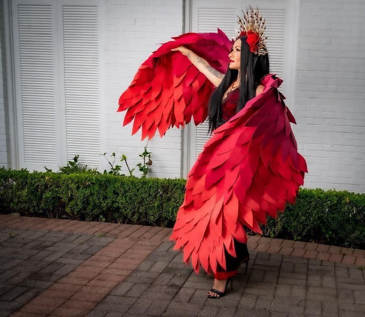 May include: A woman wearing a red and black costume with large red wings. She is wearing a crown with red flowers and has long black hair.