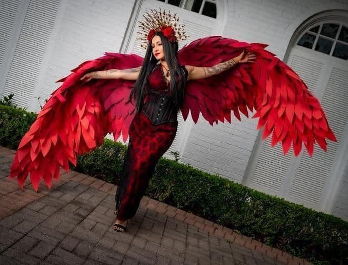 May include: A woman wearing a red and black dress with large red feathered wings and a crown of flowers on her head.