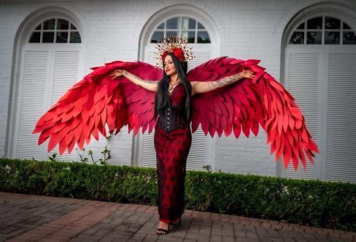 May include: A person wearing a red dress and a gold crown with red flowers, posing with large red feathered wings.