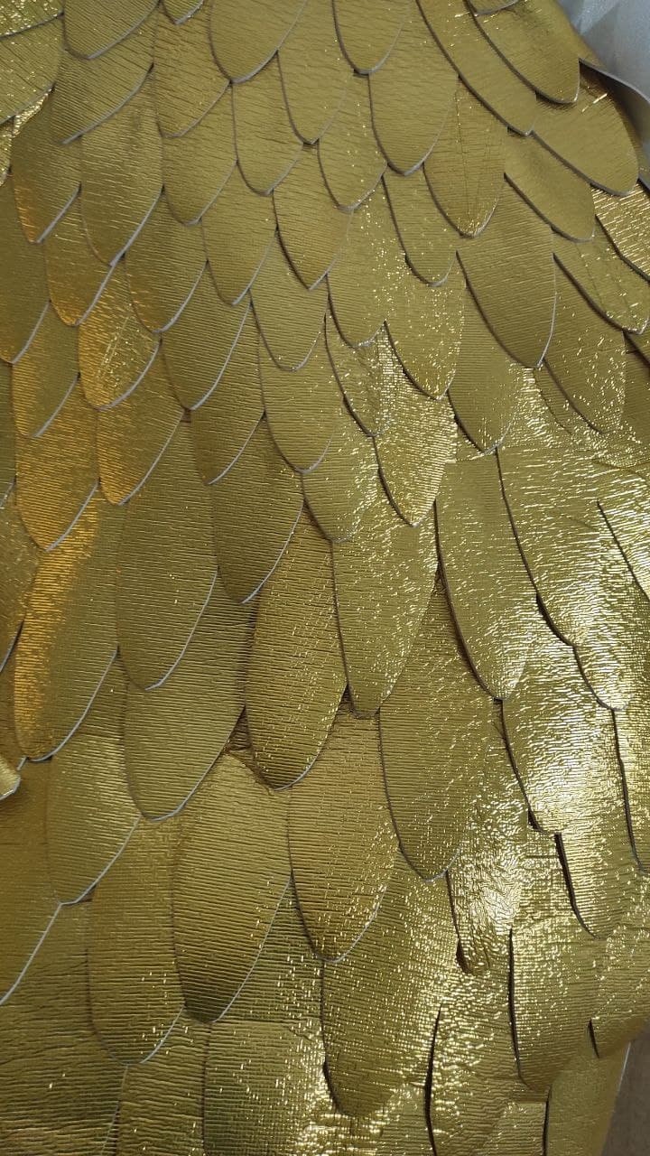 May include: A collection of overlapping, petal-shaped pieces in a metallic gold finish. Each individual piece features a textured surface and rounded edges, arranged in a repeating pattern that mimics the appearance of layered feathers or scales.