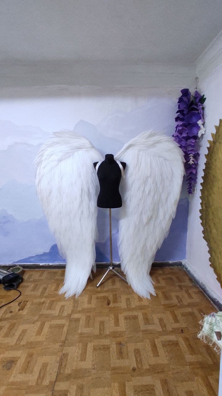 May include: A pair of large, white angel wings on a mannequin stand. The wings are made of feathers and are very detailed.