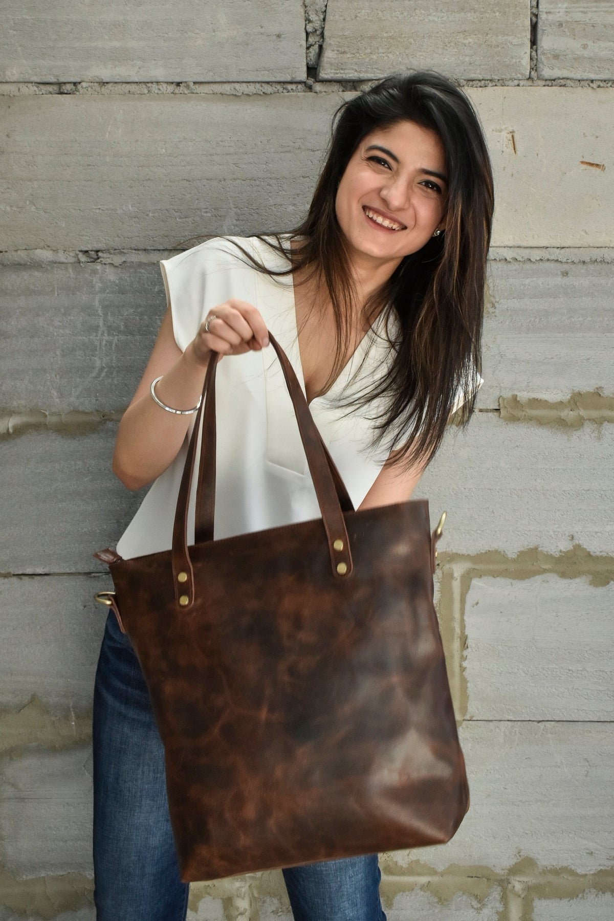 May include: A brown leather tote bag with a distressed finish and brass hardware. The bag has two top handles and a zipper closure.