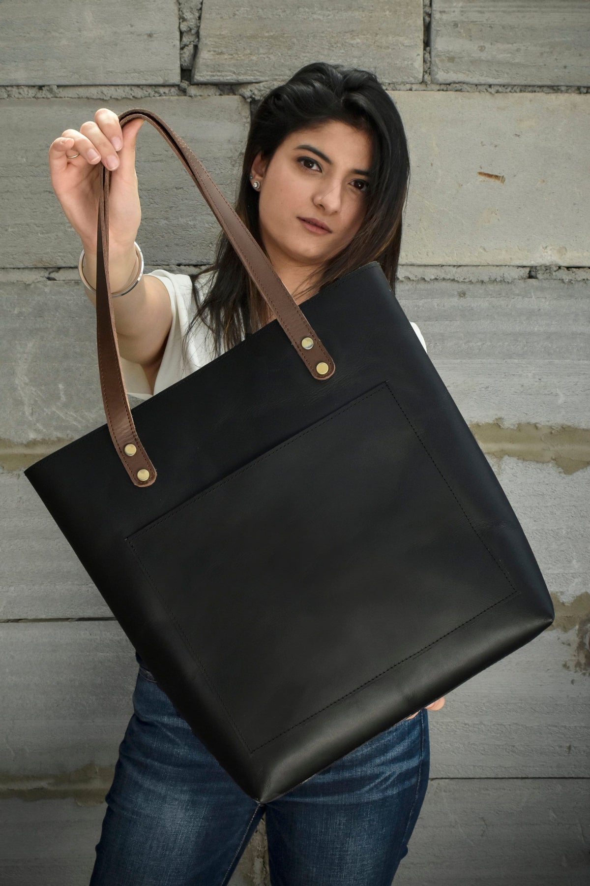 May include: A black leather tote bag with brown leather straps and a front pocket. The bag has gold metal accents.