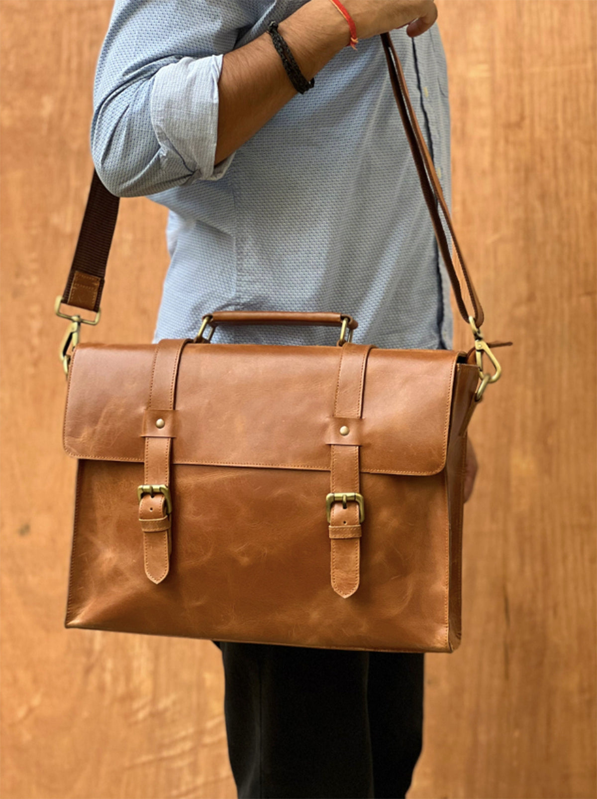 May include: A brown leather briefcase with a top handle and a shoulder strap. The briefcase has two buckles on the front and a brass clasp.
