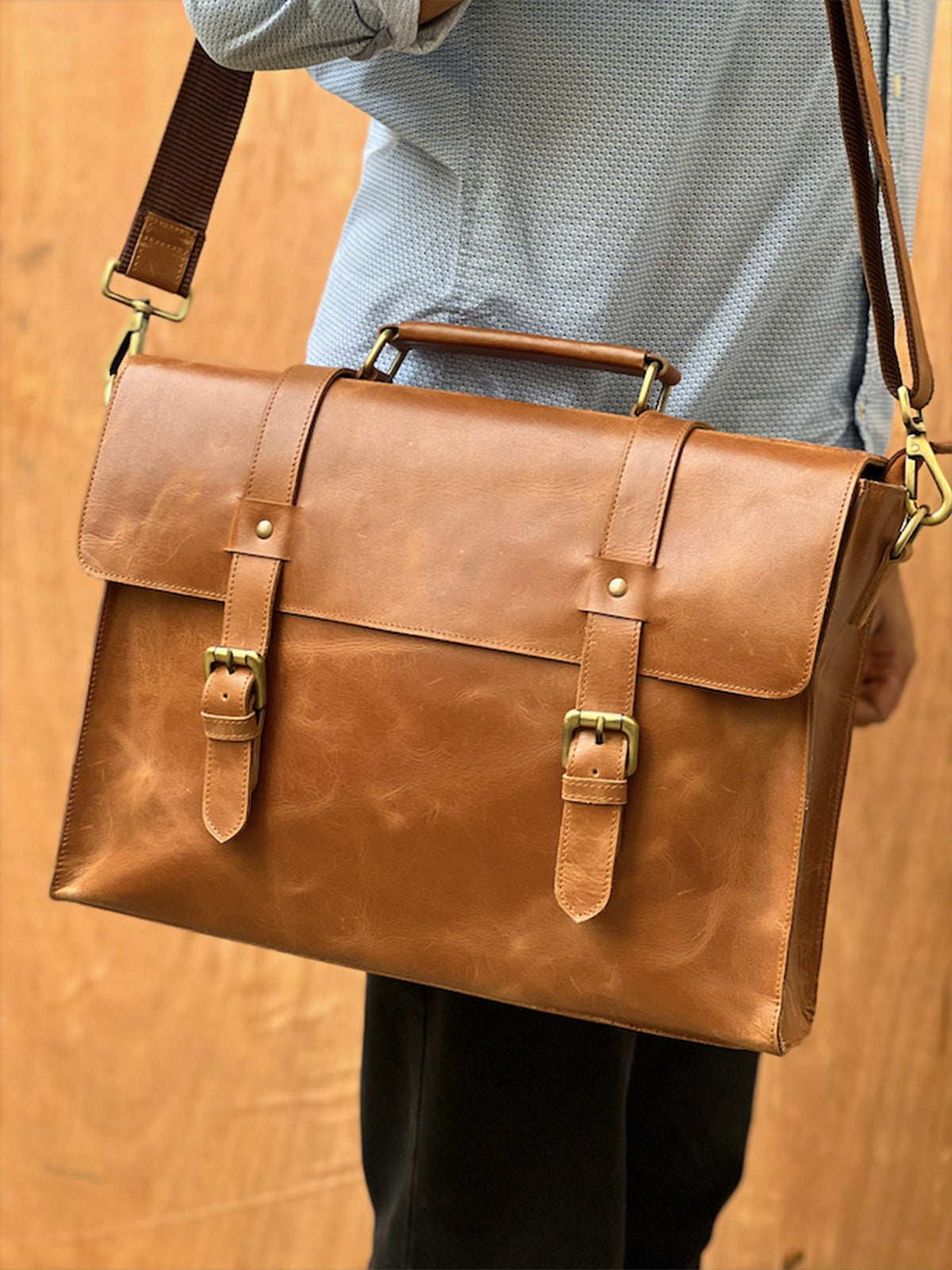 May include: A brown leather briefcase with a top handle and a shoulder strap. The briefcase has two buckles on the front and a brass clasp on the top.