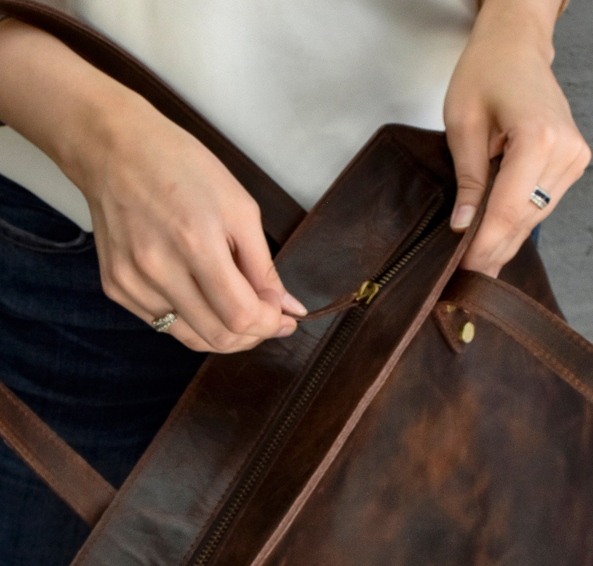 May include: A brown leather tote bag with a zipper closure and a brass buckle. The bag has a top handle and a shoulder strap.