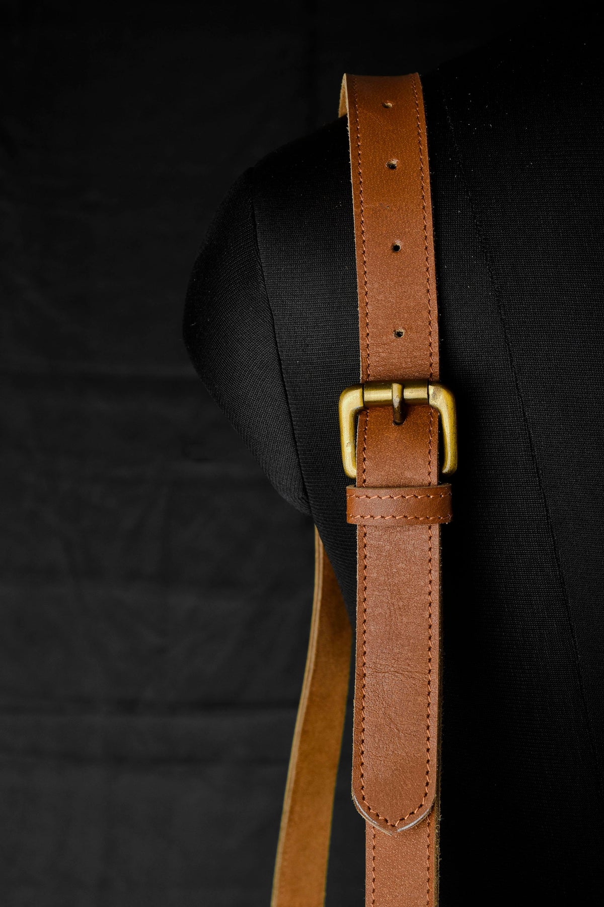 May include: A brown leather strap with a brass buckle. The strap is stitched with a decorative pattern.