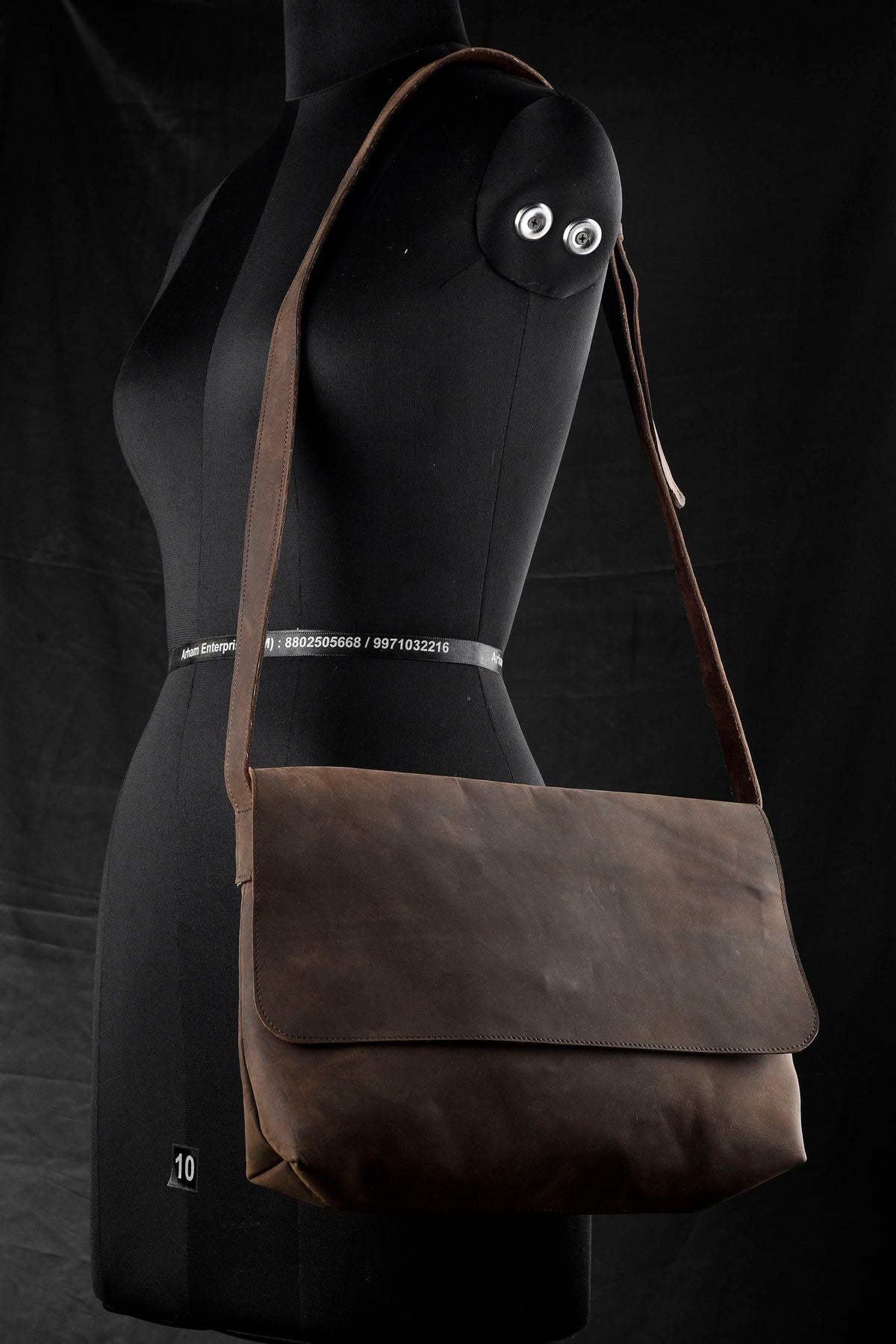 May include: A brown leather messenger bag with a flap closure and adjustable shoulder strap. The bag is shown on a black mannequin.