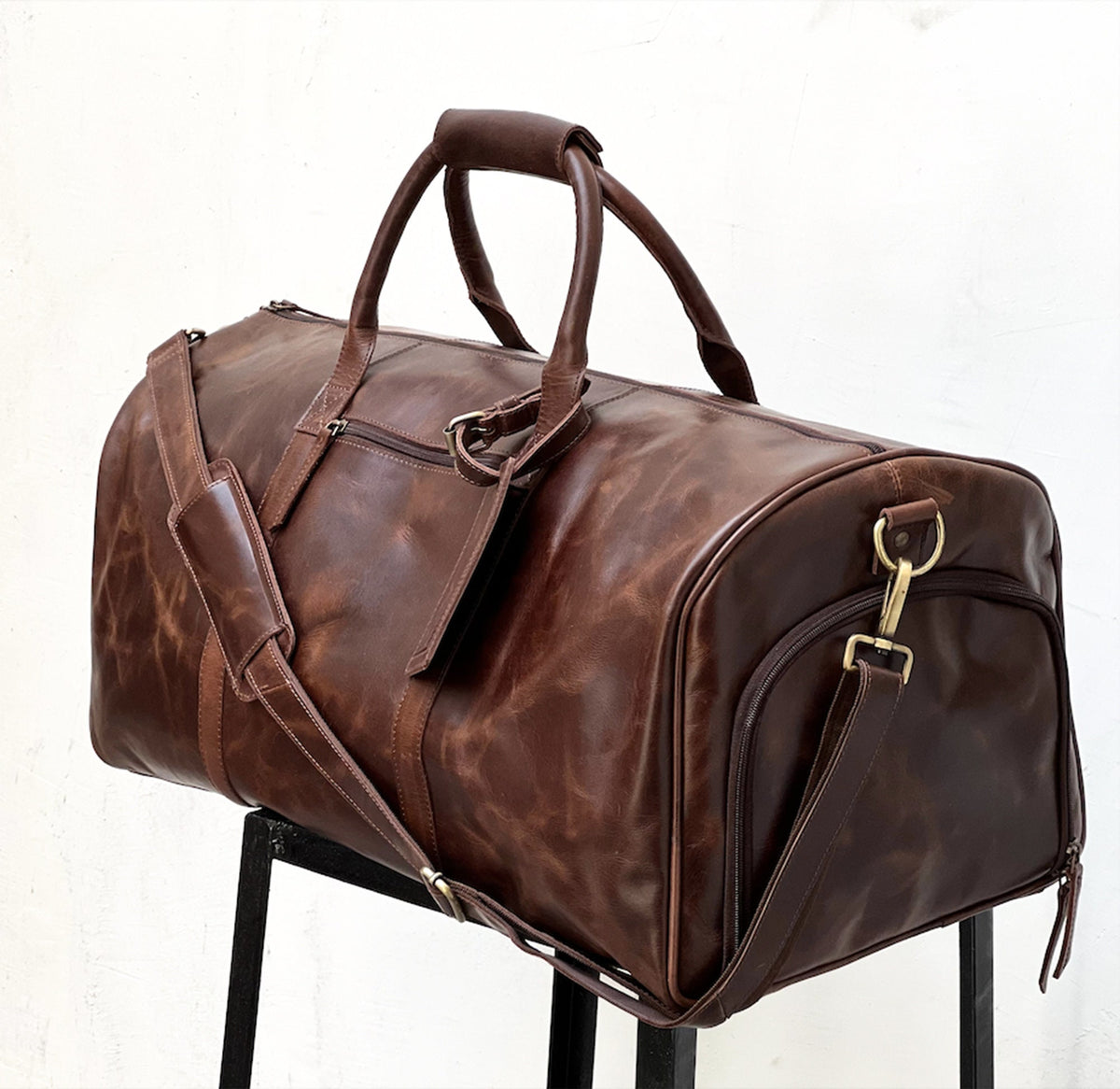 May include: A brown leather duffel bag with a top handle and a shoulder strap. The bag has a zipper closure and a gold metal buckle.
