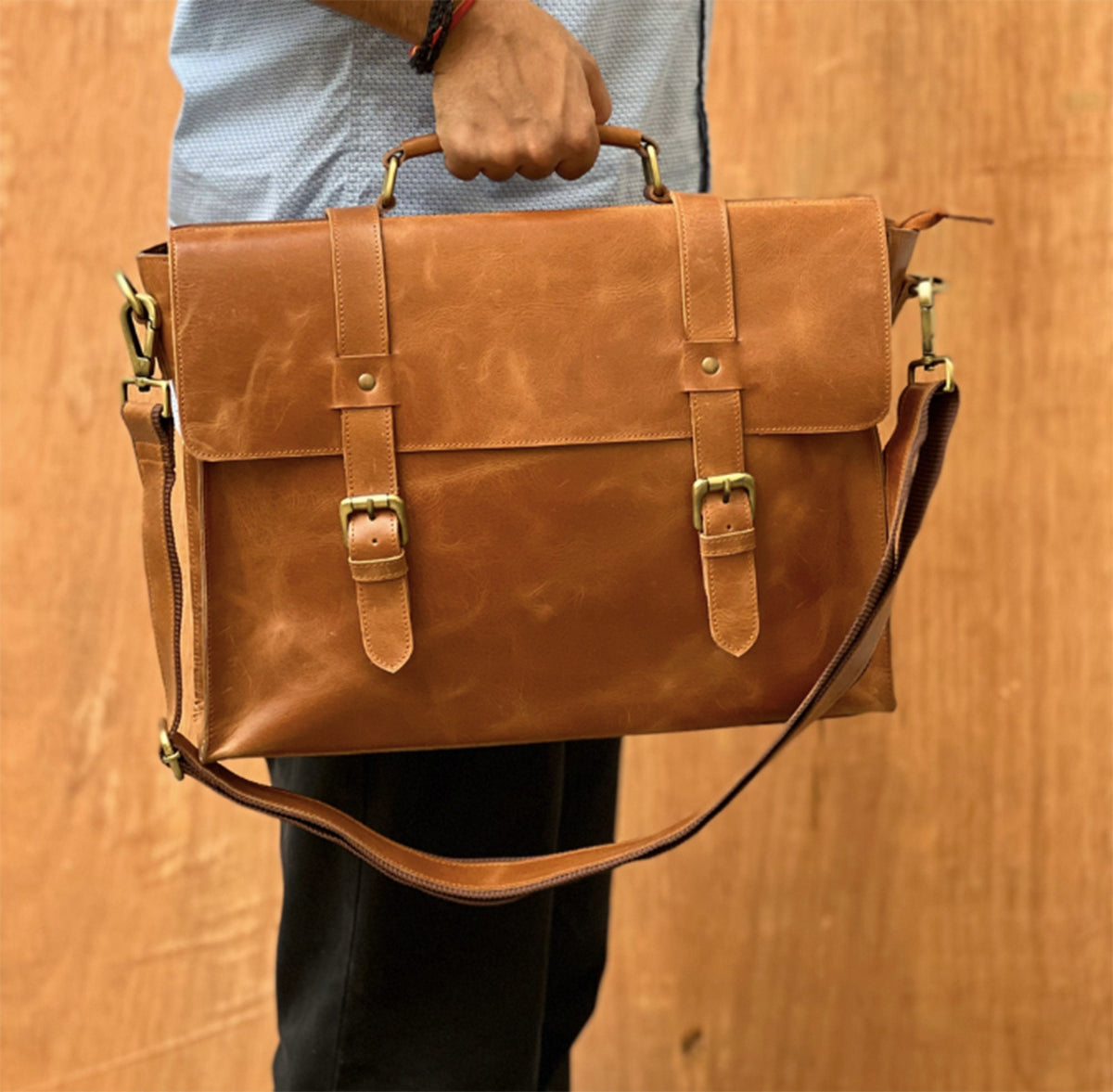 May include: A brown leather briefcase with a long strap and two buckles. The briefcase has a flap with a brass clasp.