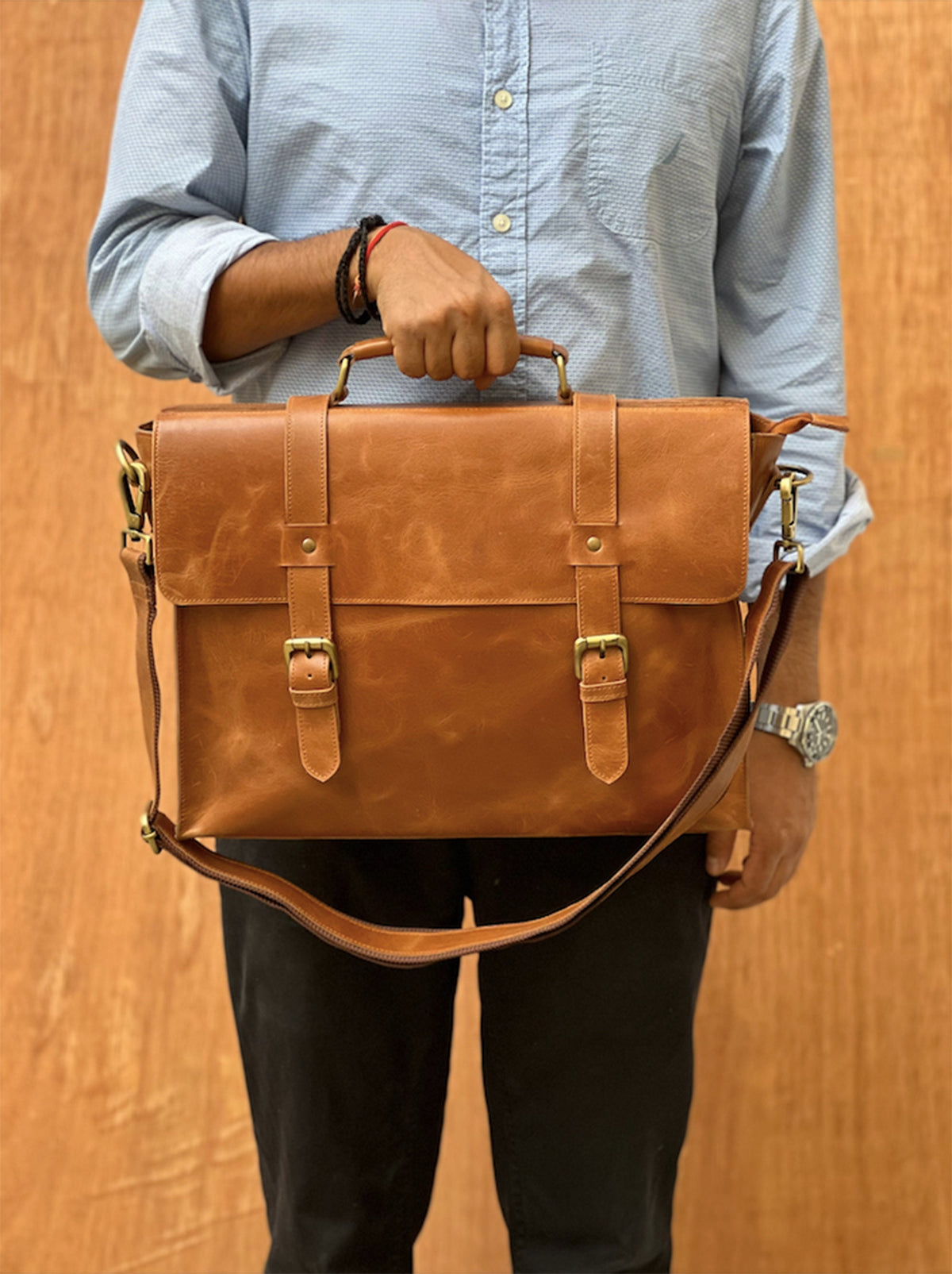 May include: A brown leather briefcase with a top handle and a shoulder strap. The briefcase has two buckles on the front and a flap that closes with a buckle.