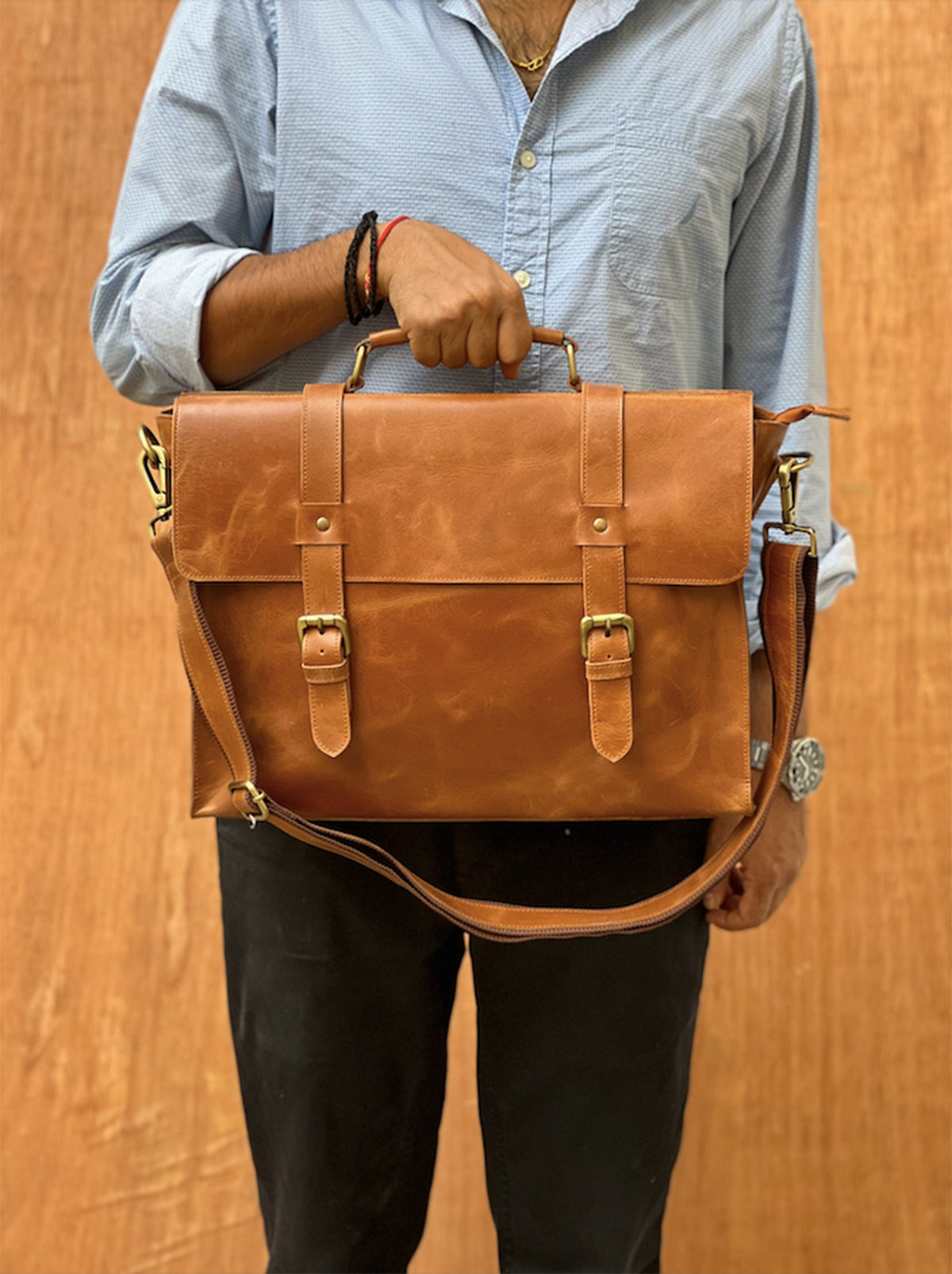 May include: A brown leather briefcase with a top handle and a shoulder strap. The briefcase has two buckles on the front and a zipper closure.