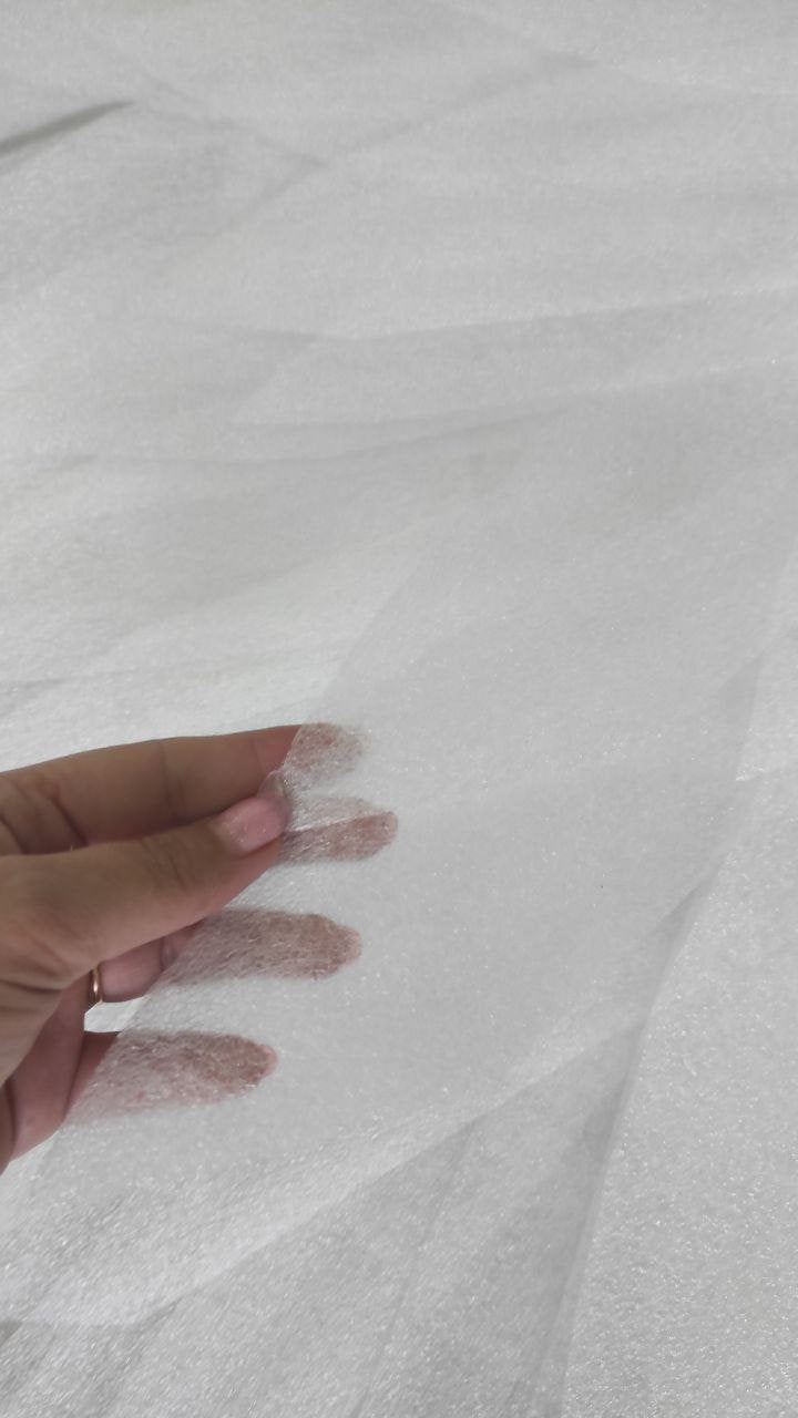 May include: Close-up of sheer white fabric, possibly tulle or netting, with a slightly textured appearance. The fabric is held in a hand, showcasing its delicate nature and potential use in crafting or fashion.