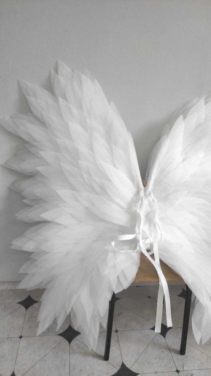 May include: White angel wings made of layered tulle fabric. The wings are tied together with white ribbon and are ready to be worn.
