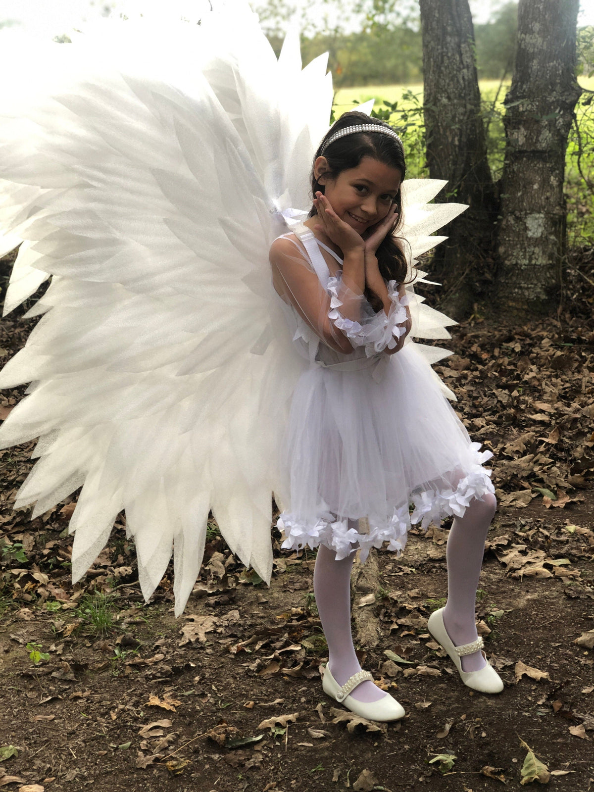 May include: A white costume featuring large, feathered-style wings, a sleeveless dress with a layered tulle skirt, white tights, and white shoes with pearl-like accents. The dress includes sheer sleeves and decorative white floral embellishments.