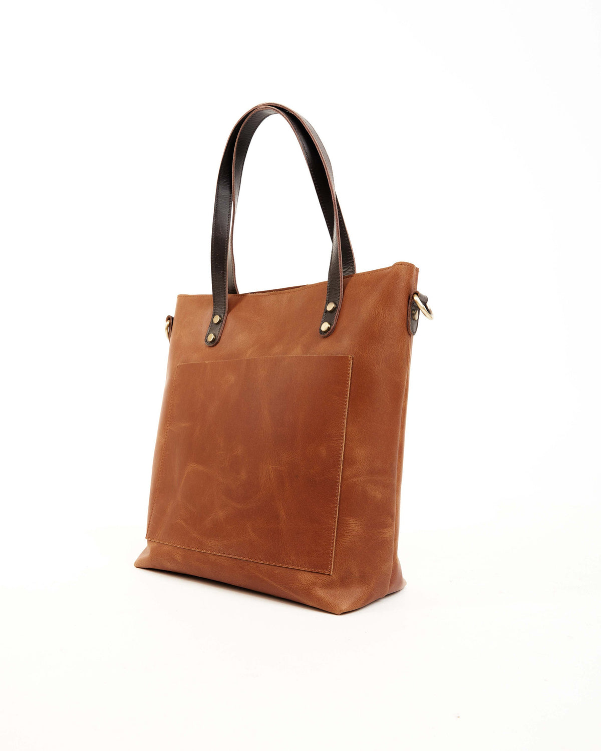 May include: A brown leather tote bag with a black leather handle and a front pocket. The bag has a brass buckle and a brass ring on the strap.