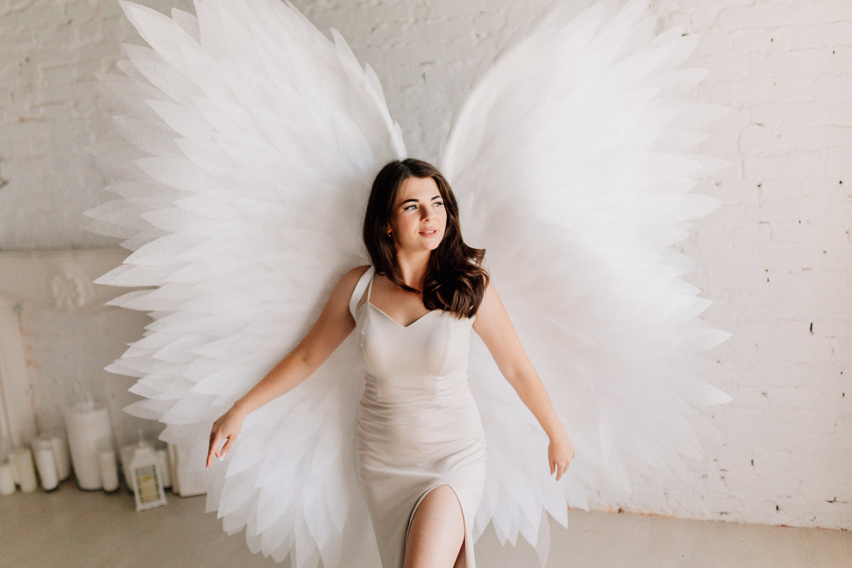 May include: A woman wearing a white dress with a slit up the leg, standing with large white angel wings behind her.