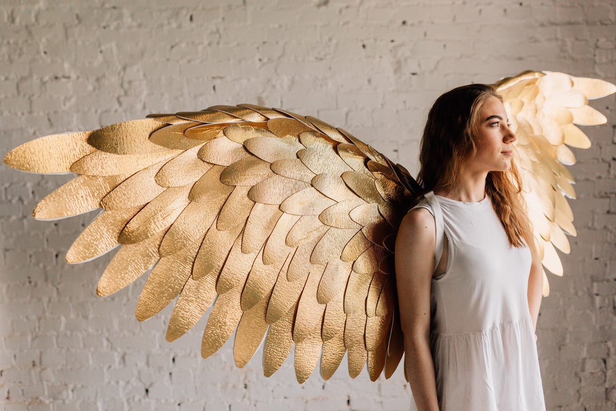 May include: A person wearing a white sleeveless dress with large, gold, feathered angel wings.