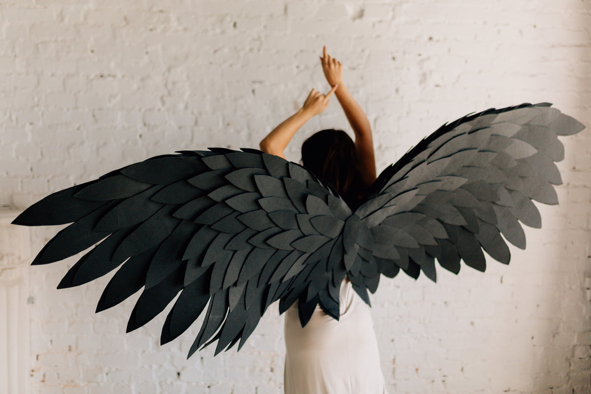 May include: A person wearing a white dress with large, black, paper wings. The wings are made of many overlapping feathers.