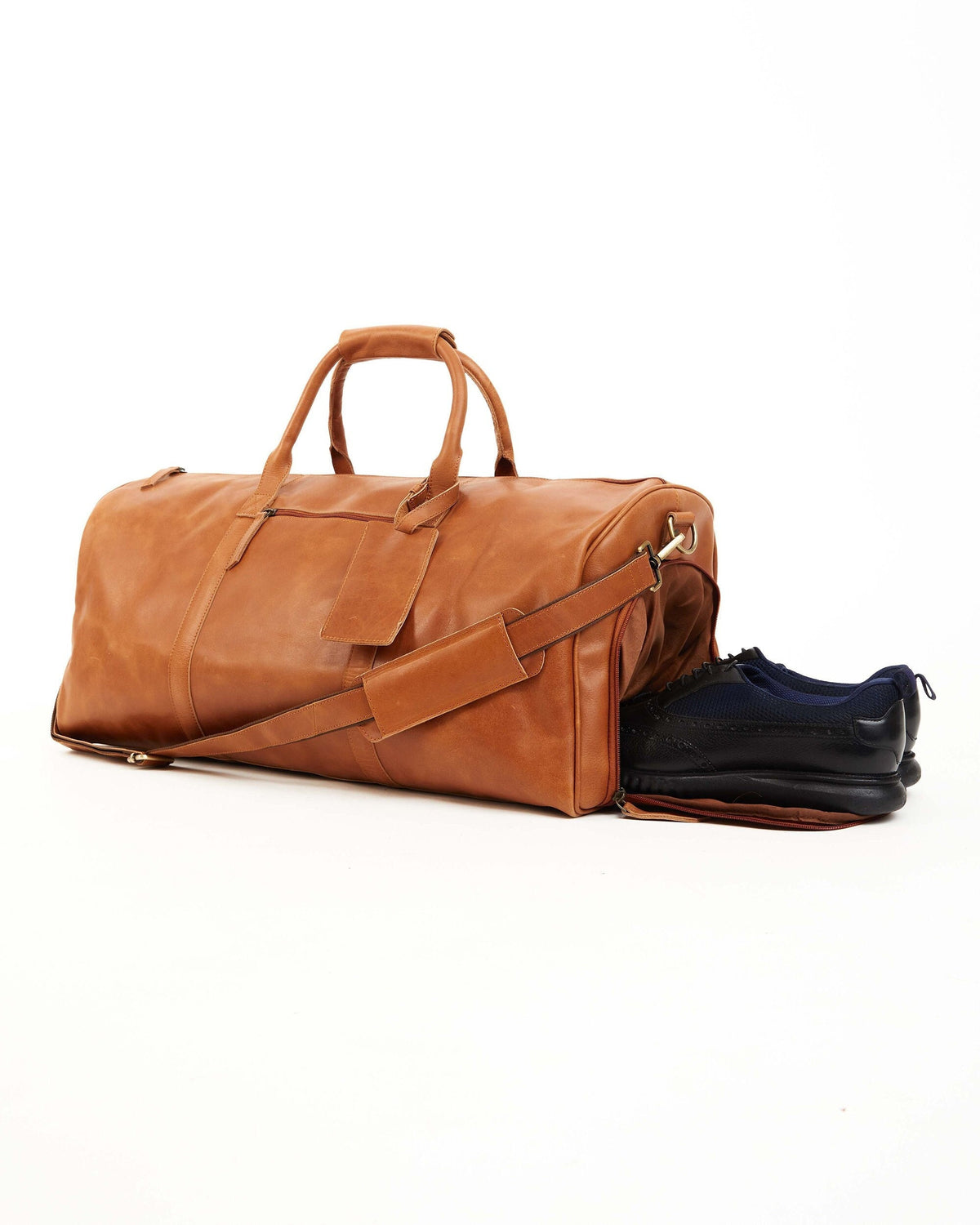 May include: A brown leather duffel bag with a top handle and a shoulder strap. The bag is open and has a pair of black shoes inside.