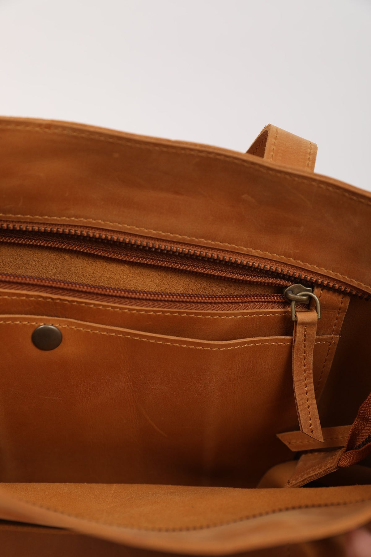 May include: The inside of a brown leather tote bag with a zippered pocket and a smaller open pocket. The bag has a brown leather strap.