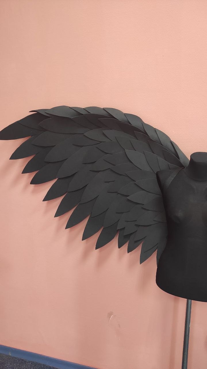 May include: Black paper angel wings with a layered, feathered design. The wings are attached to a black mannequin torso.