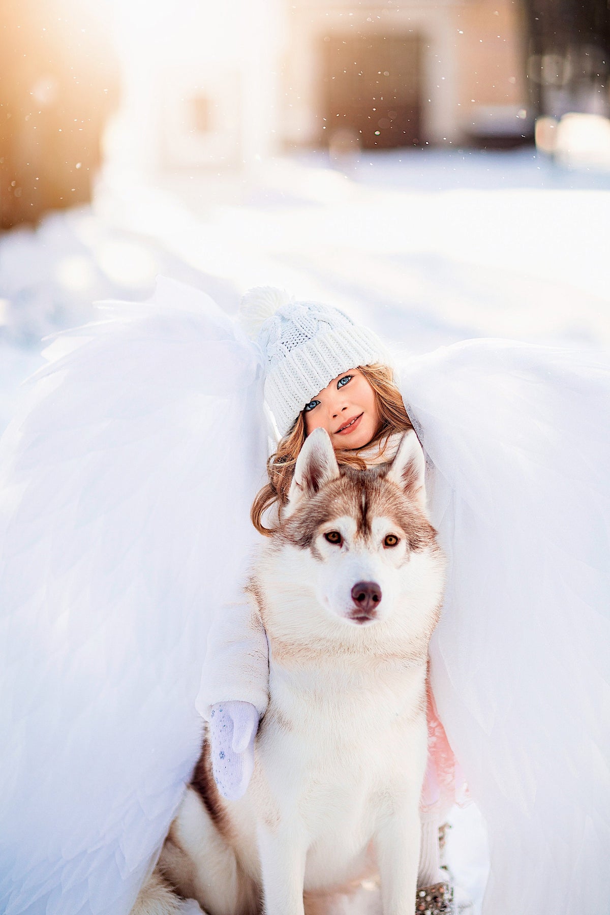 May include: A young girl wearing a white knit hat and a white coat is sitting with a Siberian Husky dog in a snowy landscape. The girl and dog are surrounded by white fabric, creating a whimsical scene.