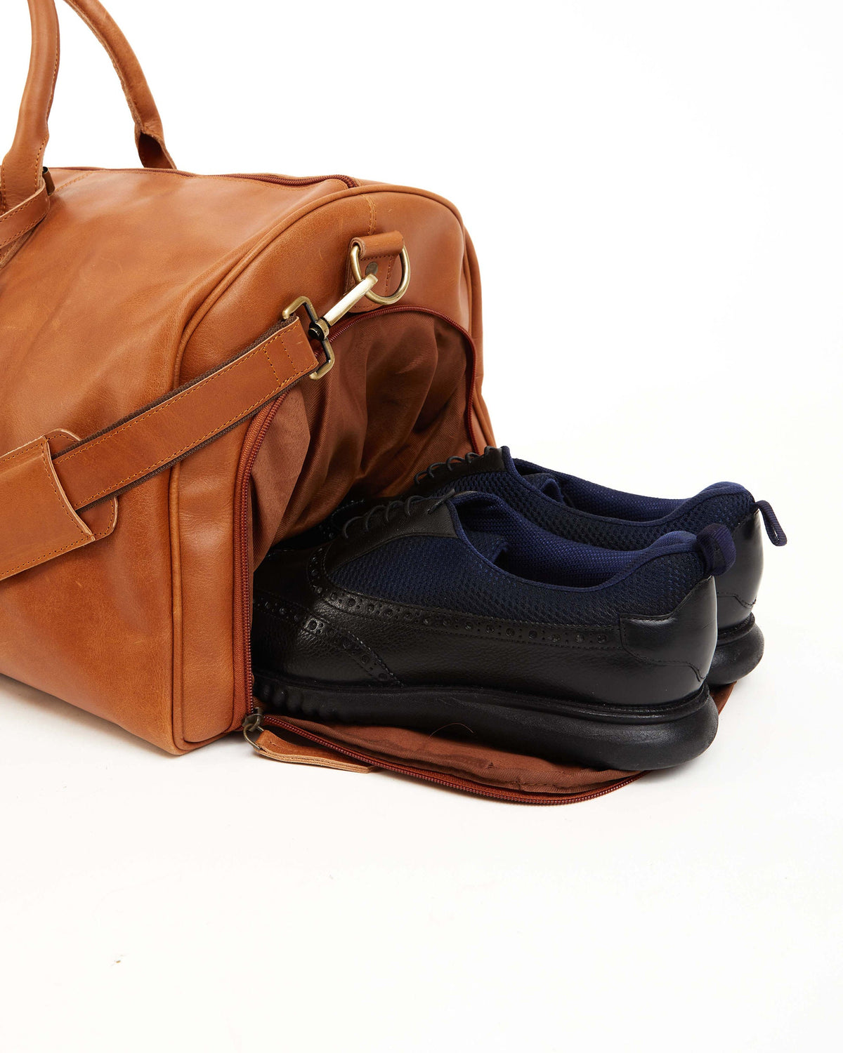May include: A brown leather duffel bag with a zippered opening. The bag is open and two black leather shoes with blue mesh panels are inside.