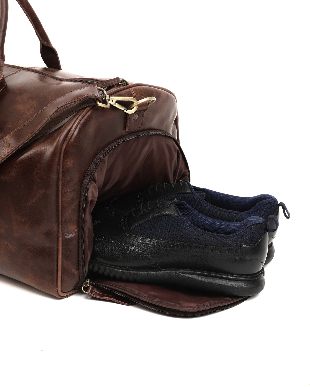May include: A brown leather duffel bag with a zippered pocket on the side. The bag is open and two black leather shoes are inside.