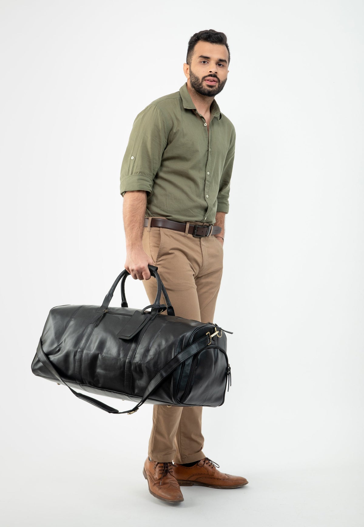 May include: A man in a green shirt and khaki pants is holding a black leather duffel bag.