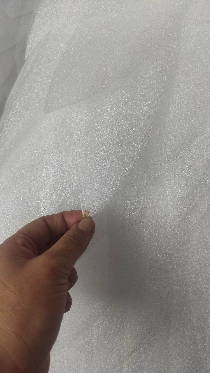 May include: A close-up of a white, textured, bubble wrap sheet. A hand is holding a piece of the bubble wrap, showing the bubbles.