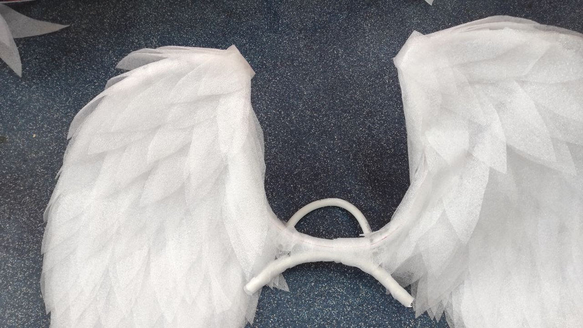 May include: A pair of white angel wings made of layered tulle fabric. The wings are attached to a white wire frame.