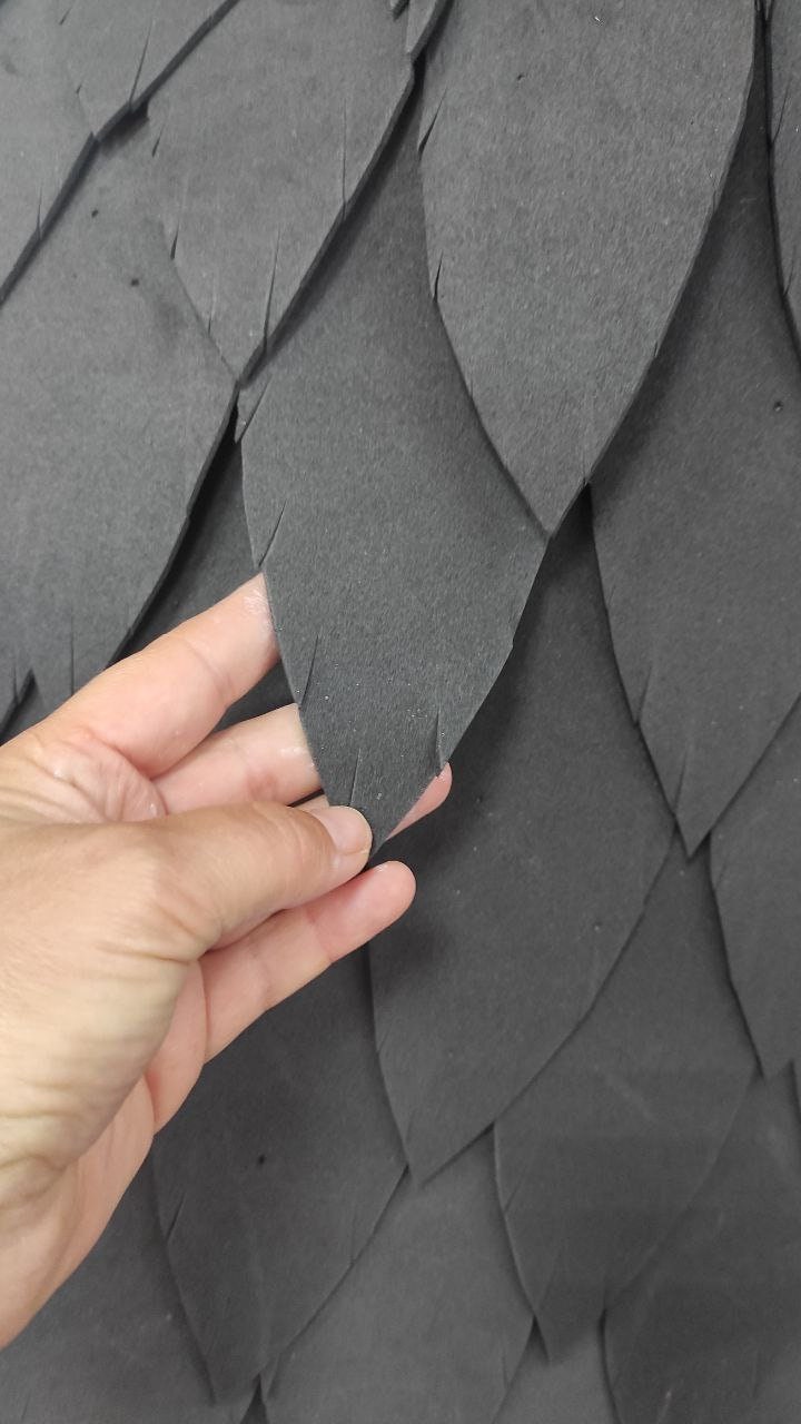 May include: Close-up of a dark gray foam material with a textured, overlapping, leaf-like pattern. The material is soft and flexible, and the leaves are arranged in a staggered pattern.