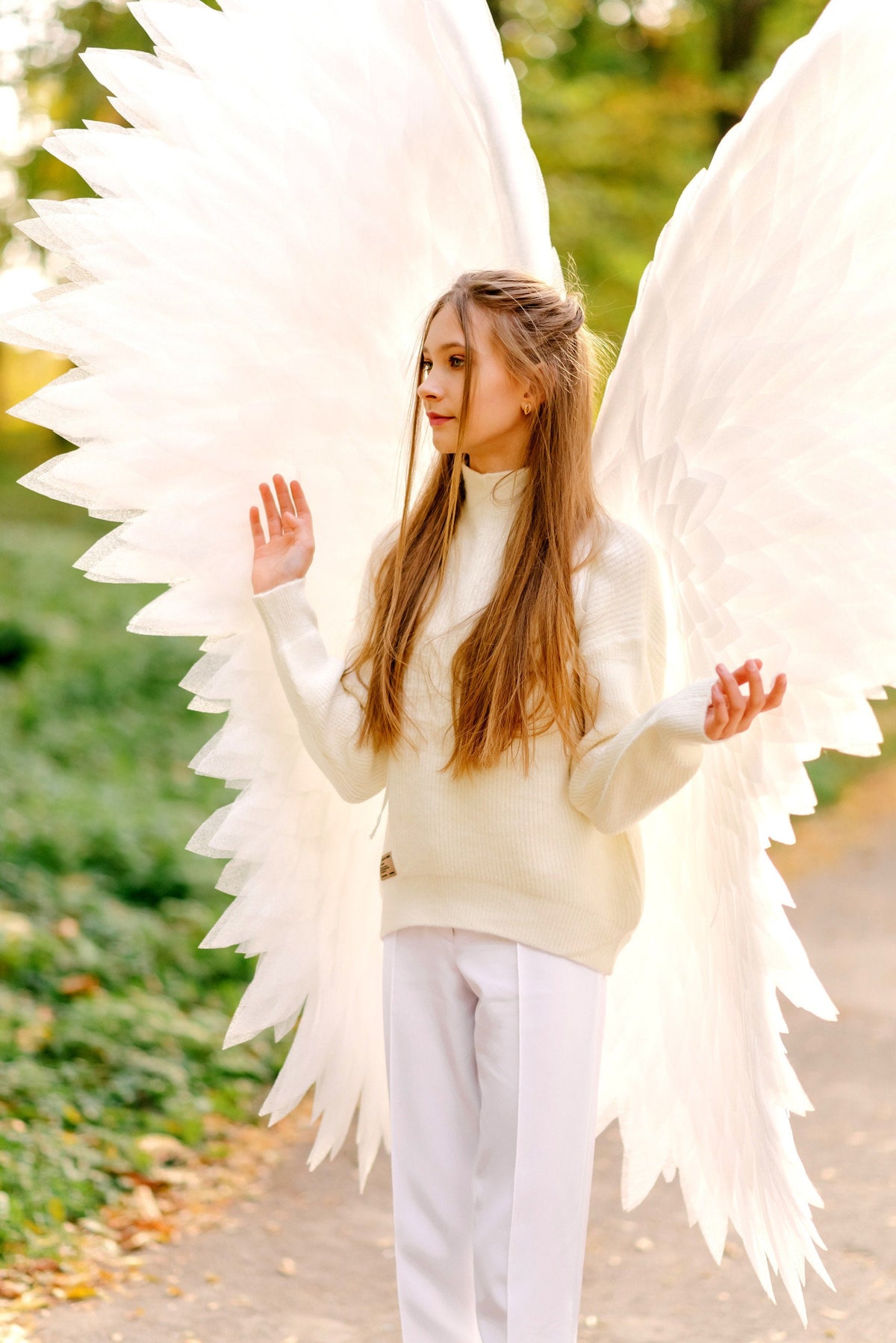 May include: A young person wearing a white sweater and white pants with large white angel wings.