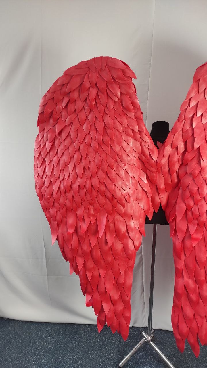 May include: Large, vibrant red costume wings. The wings are constructed from numerous individual, overlapping, petal-shaped pieces, creating a textured, feathered appearance. The wings are displayed on a black mannequin.
