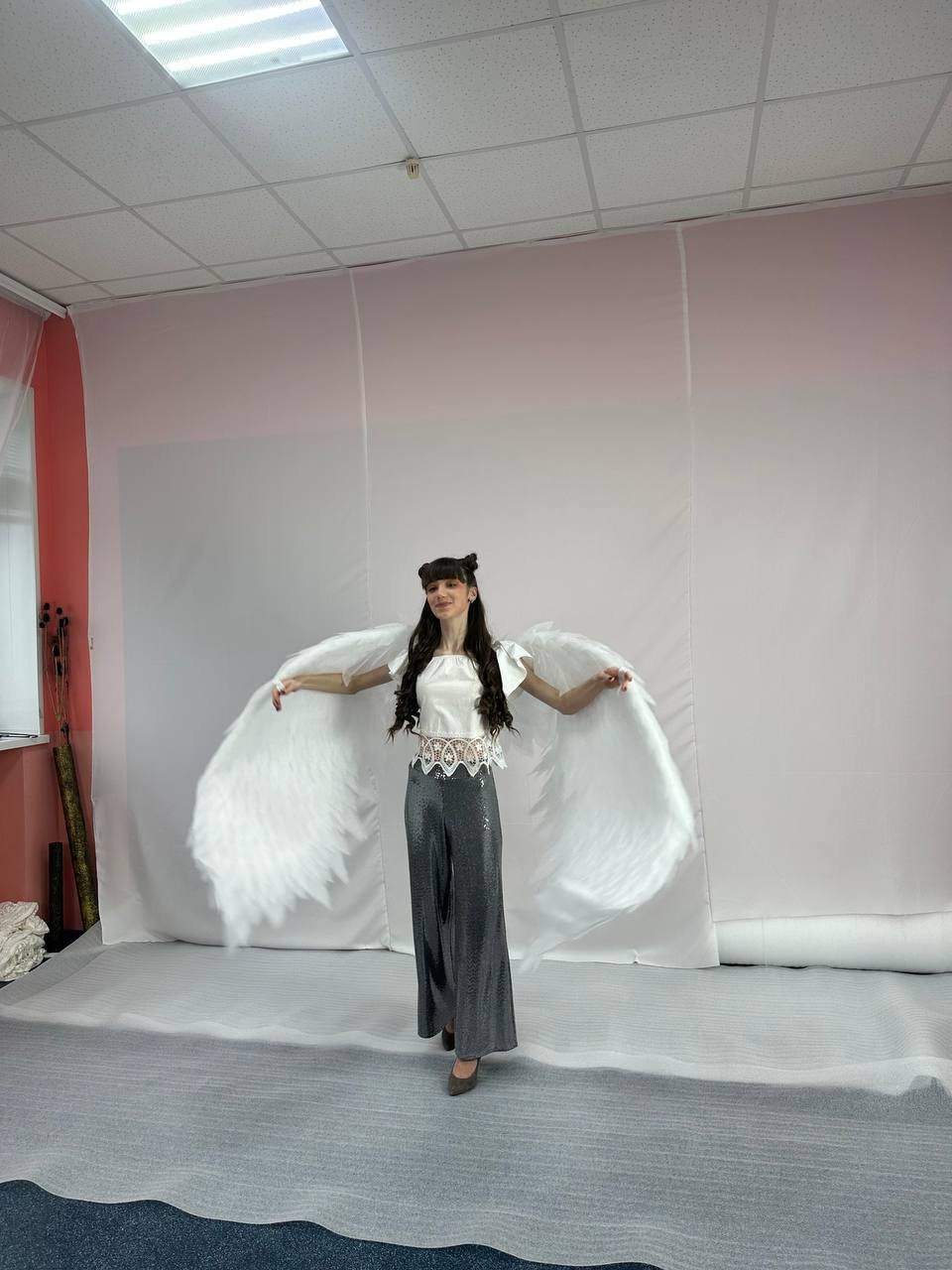May include: A person wearing a white top and gray pants with large white feathered angel wings.