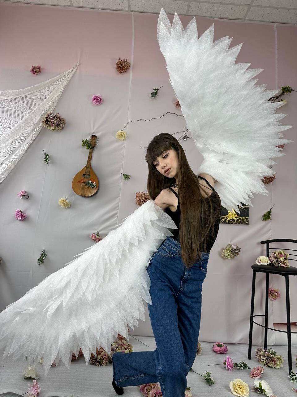 May include: A person wearing a black tank top and blue jeans with large white feathered angel wings.