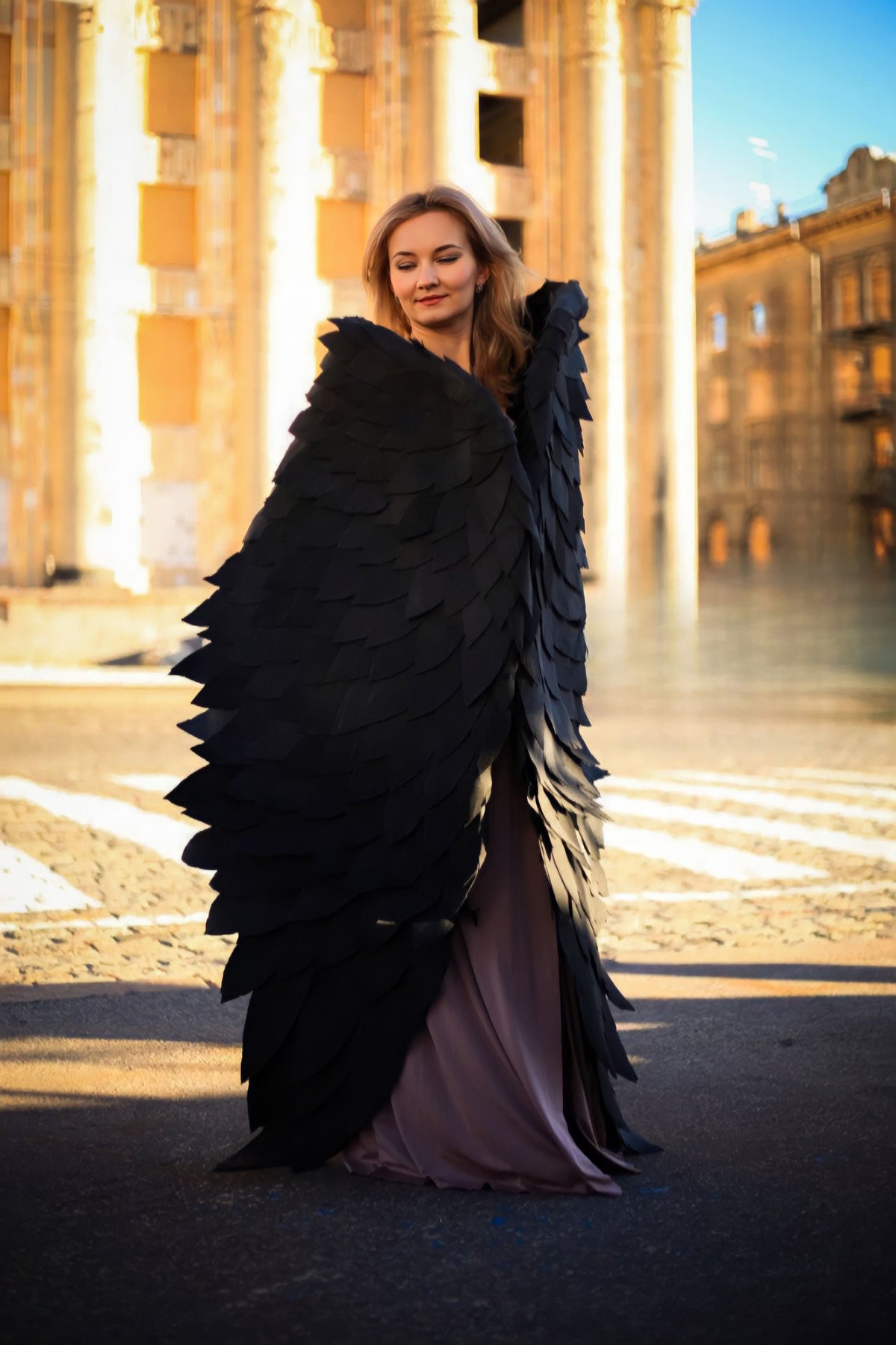 May include: A woman wearing a long, flowing, mauve dress with large, black, feathered wings.